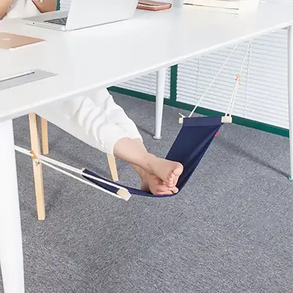 Person using a small foot hammock under a desk on a gray floor.