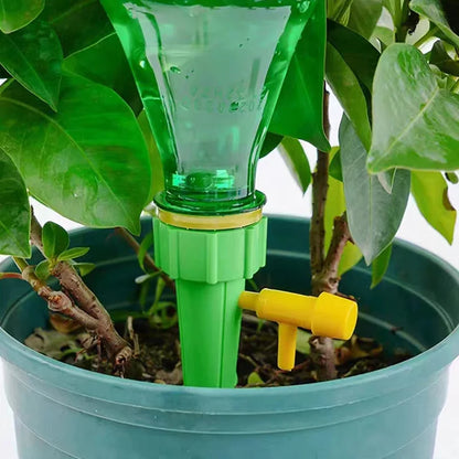 Green and yellow plant watering device in a pot with green leaves.