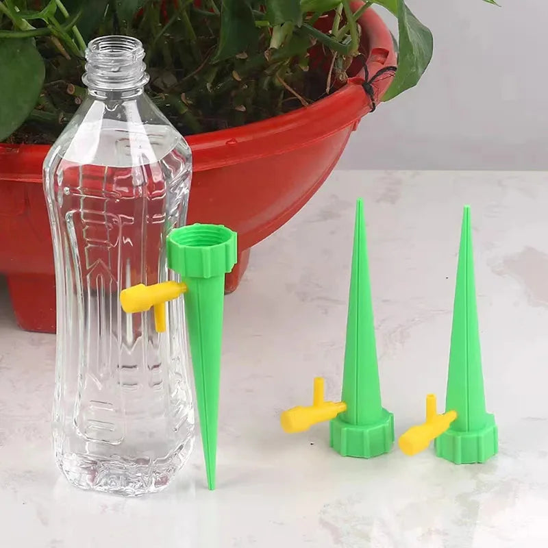 Clear bottle with green and yellow nozzles on a white surface, with a red pot and plant in the background.