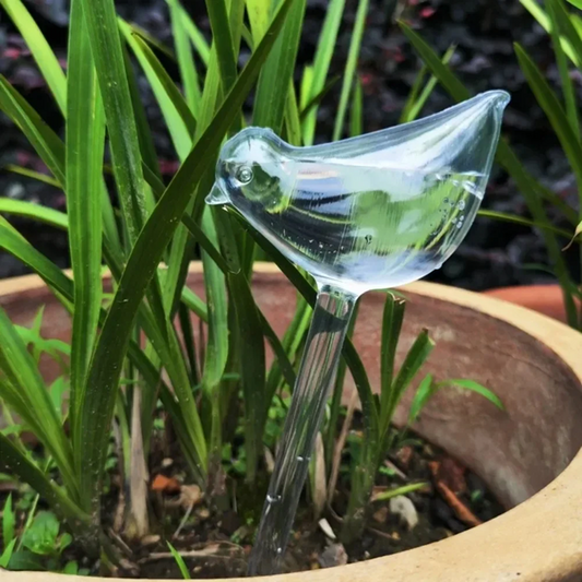 Clear glass bird-shaped water dropper in a pot with plants