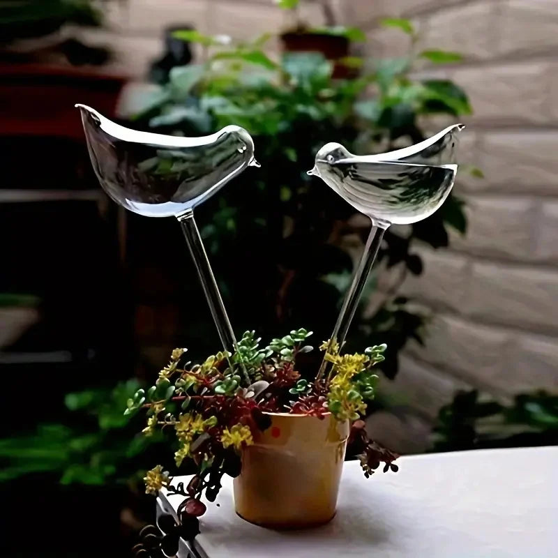 Two glass bird-shaped planters with a small potted plant on a table.