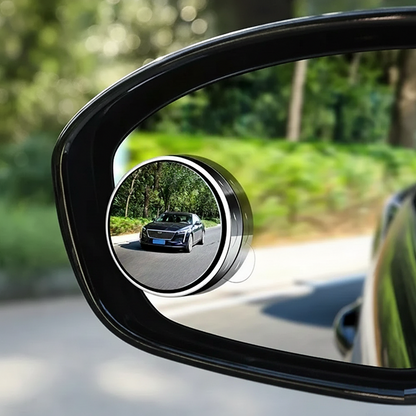 Car side mirror with a convex mirror attachment reflecting another car on a road.