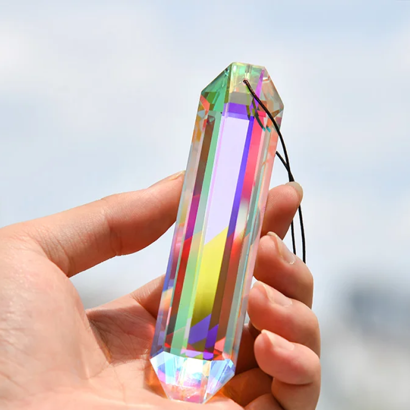 Hand holding a colorful crystal prism against a blurred natural background