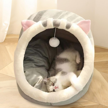 Cat lying in a gray pet bed with cat ears on a wooden floor.