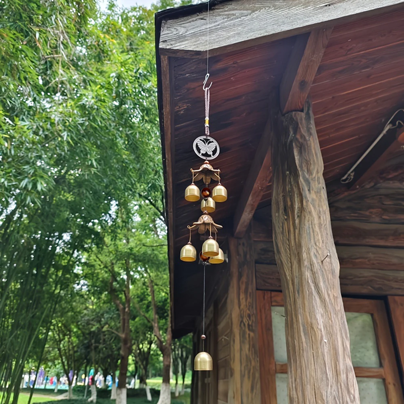 Decorative wind chime hanging from a wooden roof with trees in the background