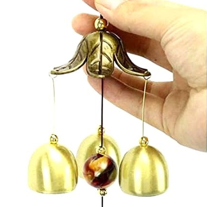 Hand holding a brass wind chime with a white background