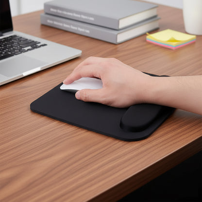 Hand using a computer mouse on a black mouse pad with a laptop and books in the background.