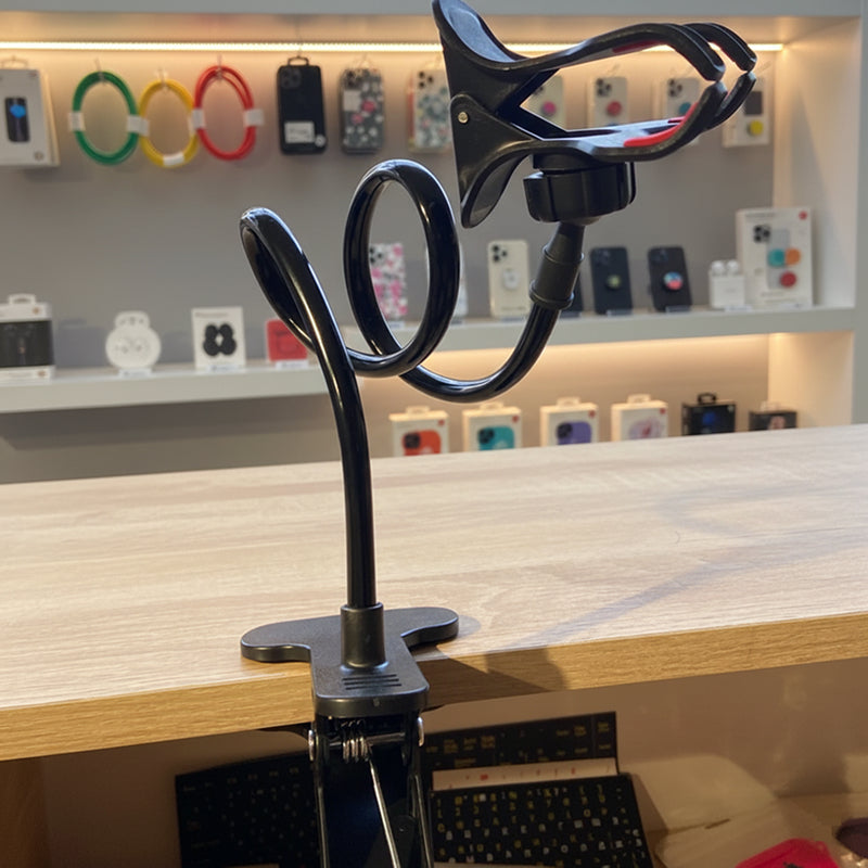 Black adjustable phone holder on a wooden surface with a store interior in the background