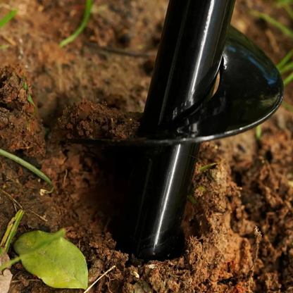 Black gardening tool digging into soil with green leaves in the background