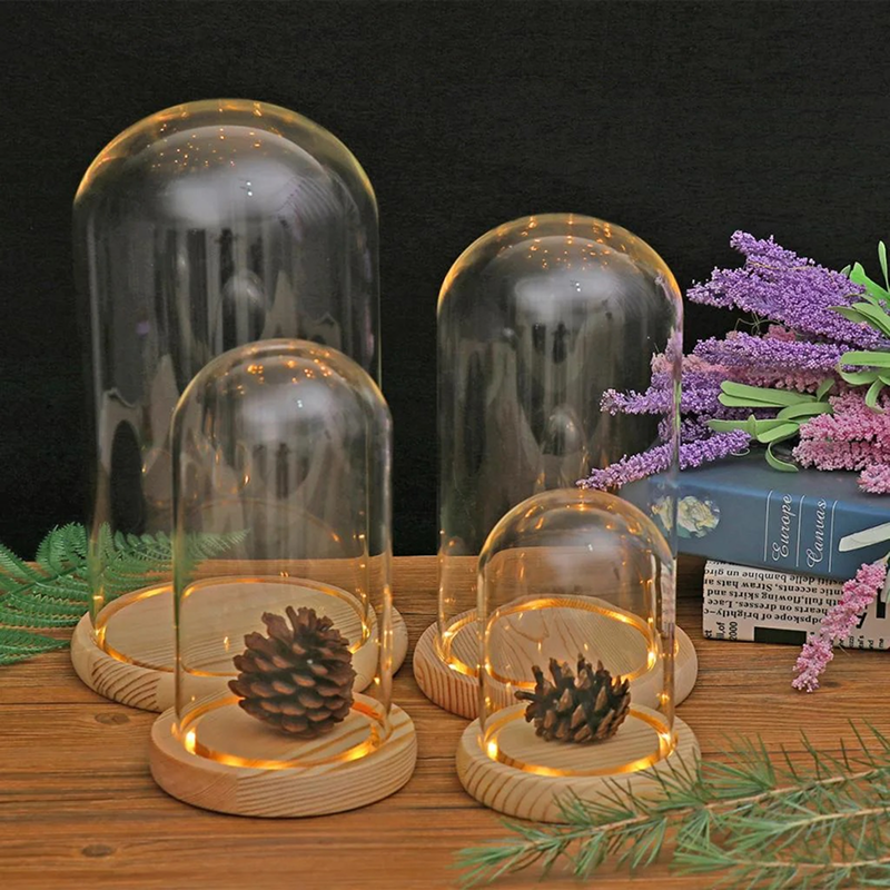 Set of glass domes with wooden bases on a wooden surface, featuring decorative elements like pinecones and lavender.