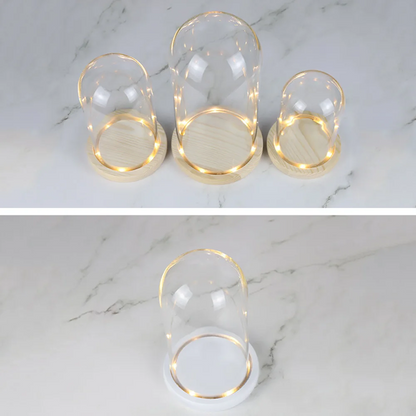 Set of three glass candle holders with wooden bases on a marble surface.