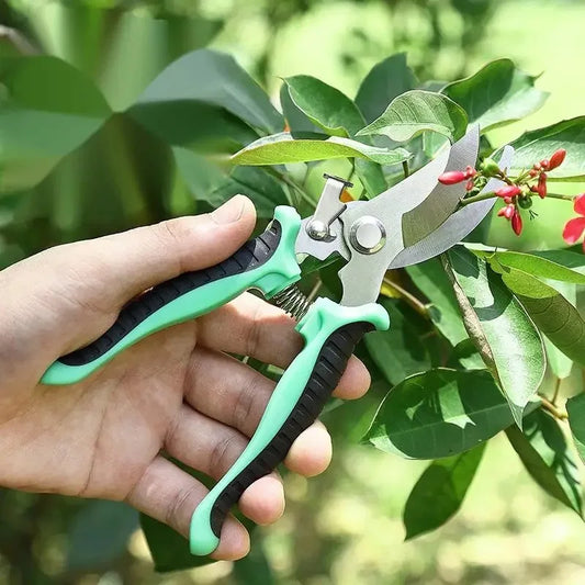 Hand holding garden shears with green handles against a background of leaves and flowers