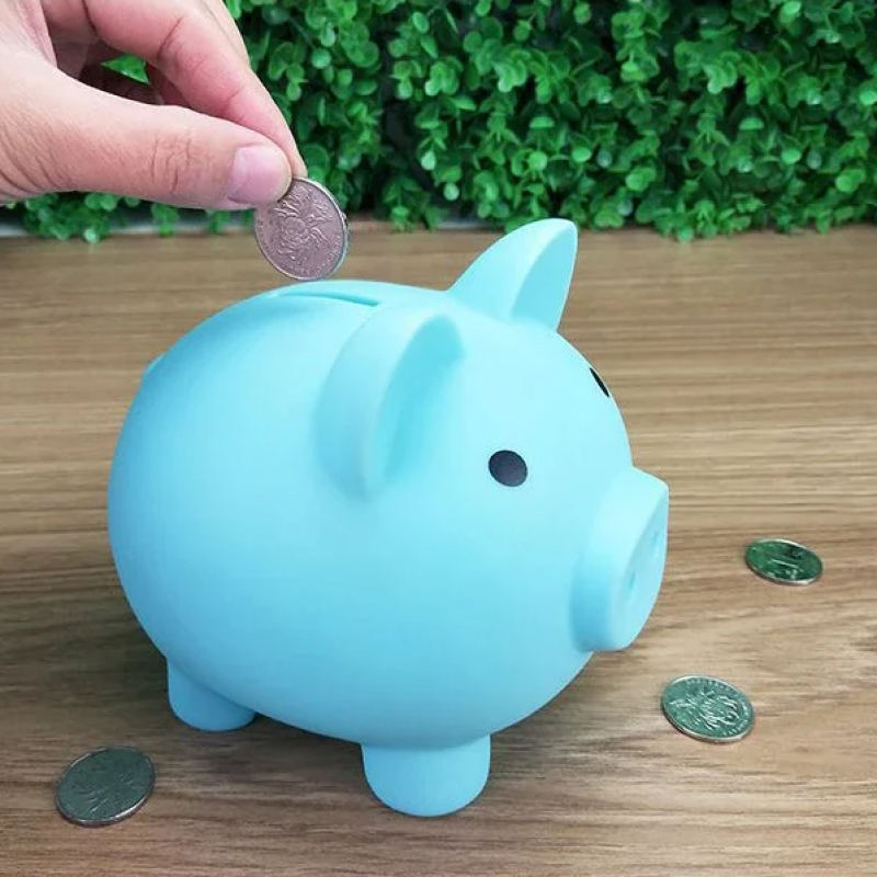 Blue piggy bank with coins on a wooden surface and green plants in the background