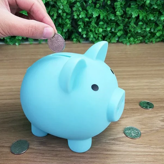 Blue piggy bank with coins on a wooden surface and green plants in the background