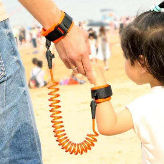 Person holding a child's hand with an orange coiled leash on a beach.