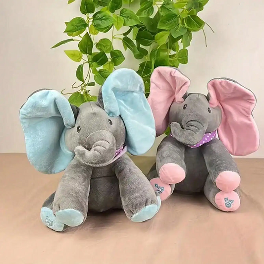 Two plush elephants, one with blue ears and the other with pink ears, on a beige surface with green leaves in the background.