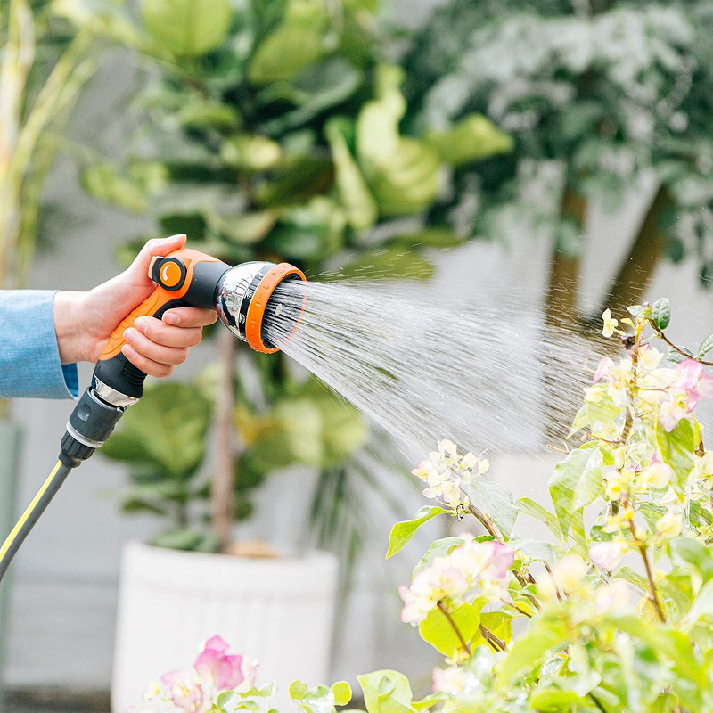 Person watering plants with a garden hose in a garden setting