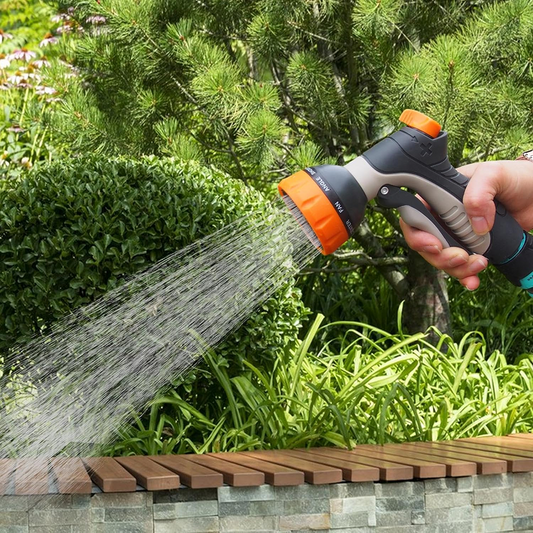 Person using a garden hose to water plants with a green background