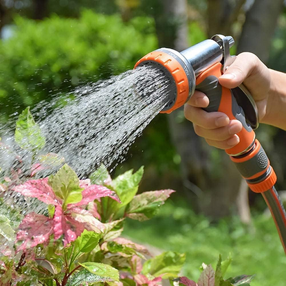 Hand holding a garden hose nozzle watering plants with a blurred green background
