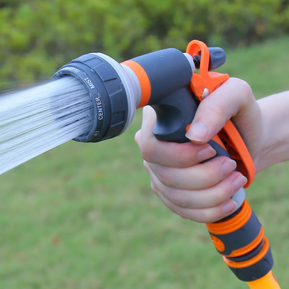 Hand holding an orange and gray garden hose nozzle with water spraying outdoors.
