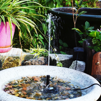 Small water fountain in a garden setting with plants and rocks.