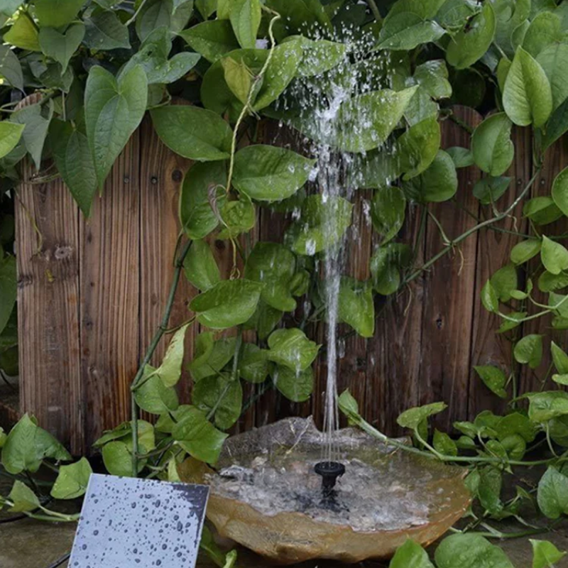 Small water fountain surrounded by green foliage with a wooden background