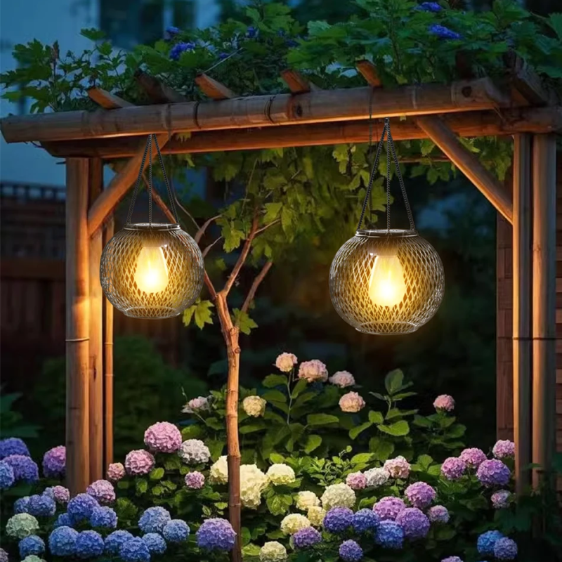 Two hanging garden lights illuminating a wooden pergola and flowers at night.