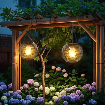 Two hanging garden lights illuminating a wooden pergola and flowers at night.