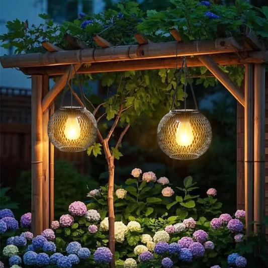 Two hanging garden lights illuminating a wooden pergola and flowers at night.