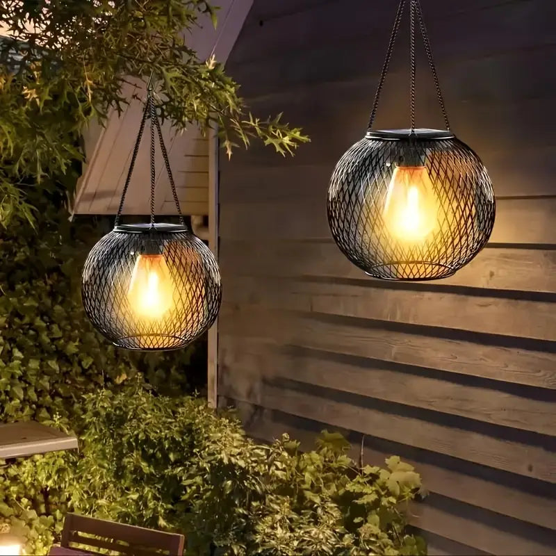 Two hanging outdoor lights with mesh design on a wooden wall and greenery.