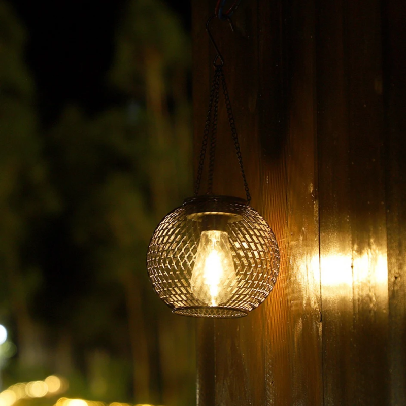 Decorative hanging light fixture on a wooden post with blurred greenery in the background