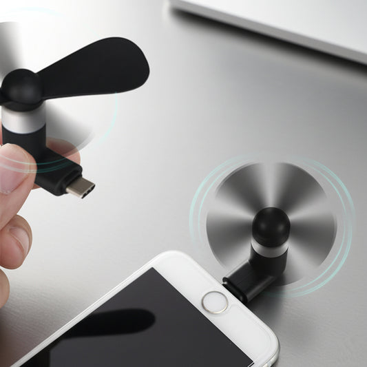 Hand holding a small USB fan attached to a smartphone on a metallic surface.