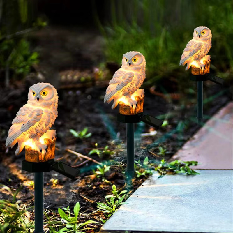 Three owl-shaped garden lights on stakes in a garden setting.