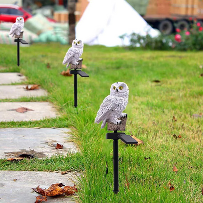 White owl statues on black stands in a grassy area with blurred background