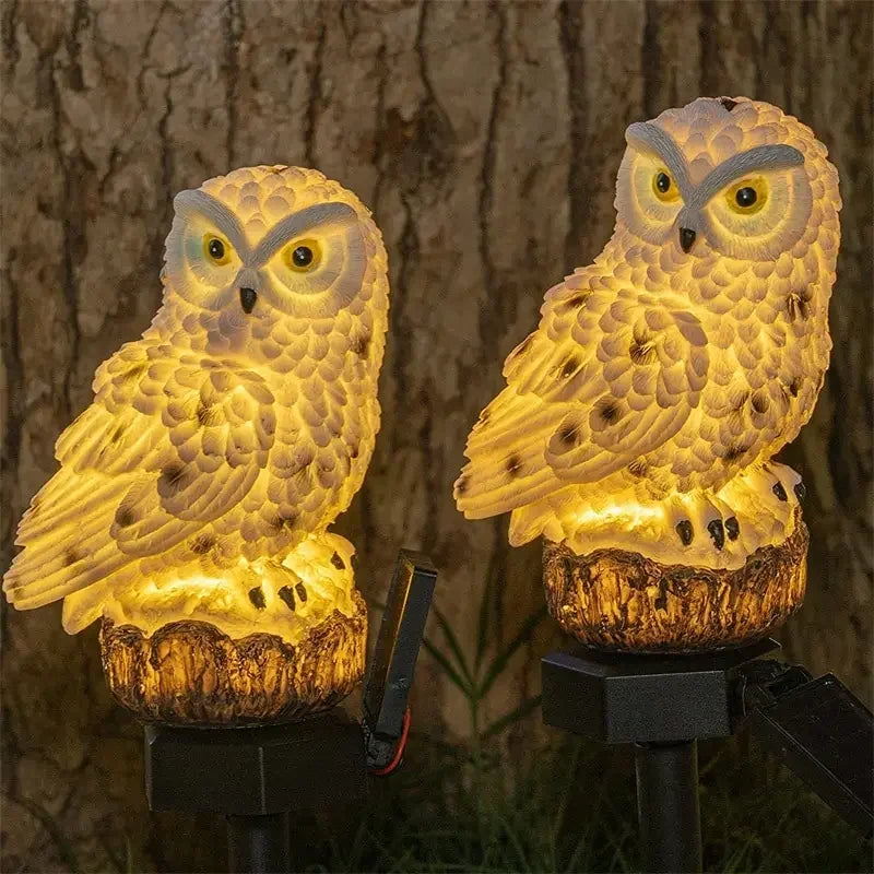 Two owl-shaped lights on stands against a tree bark background