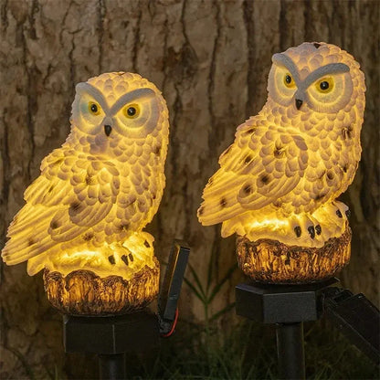 Two owl-shaped lights on stands against a tree bark background