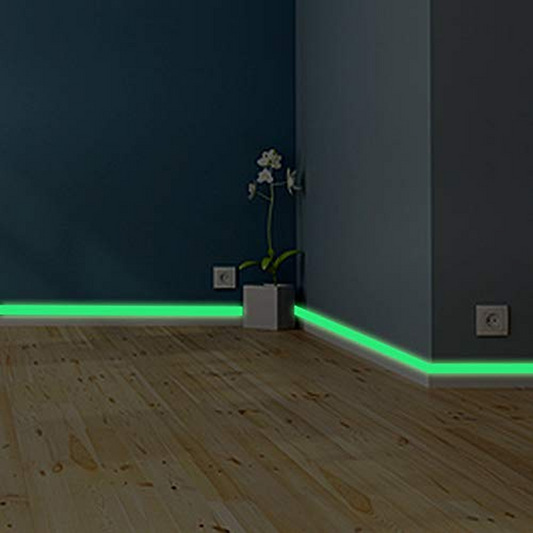 Room corner with green LED strip lights on a wooden floor and dark walls.