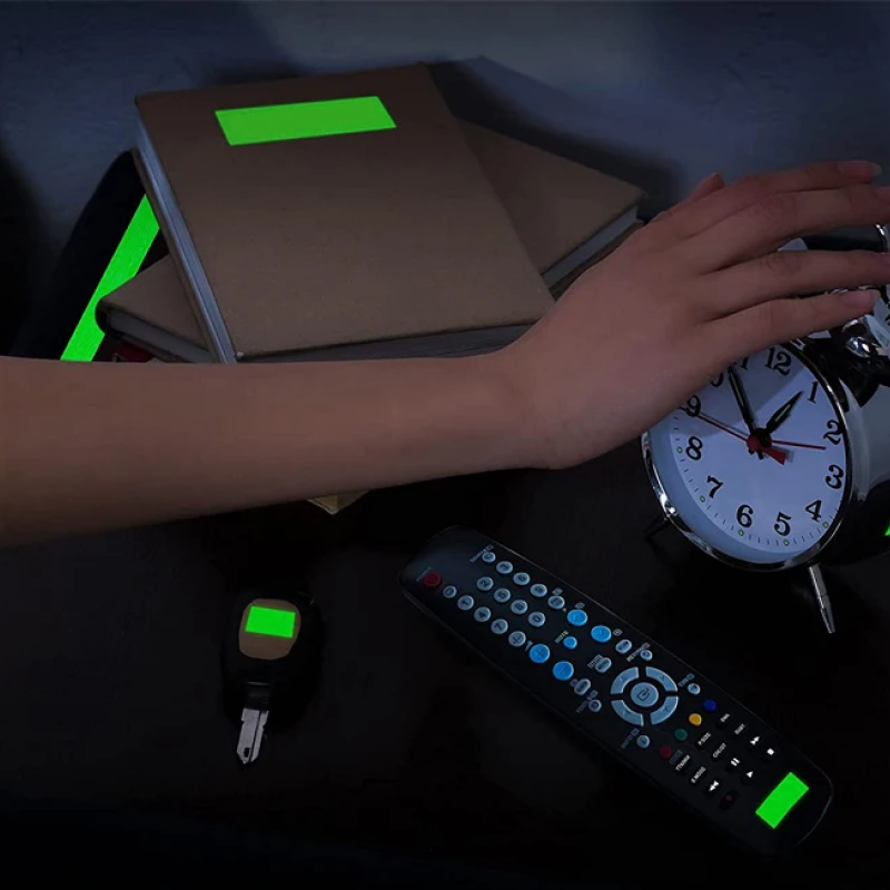 Hand adjusting an alarm clock on a dark surface with books and a remote control.