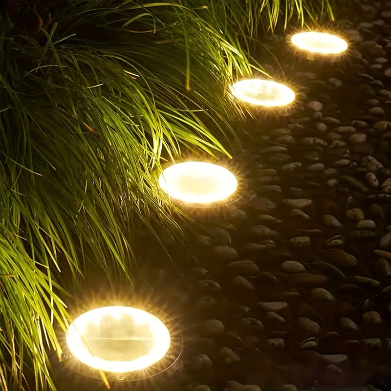 Solar-powered outdoor lights embedded in a stone pathway with grass on the side.