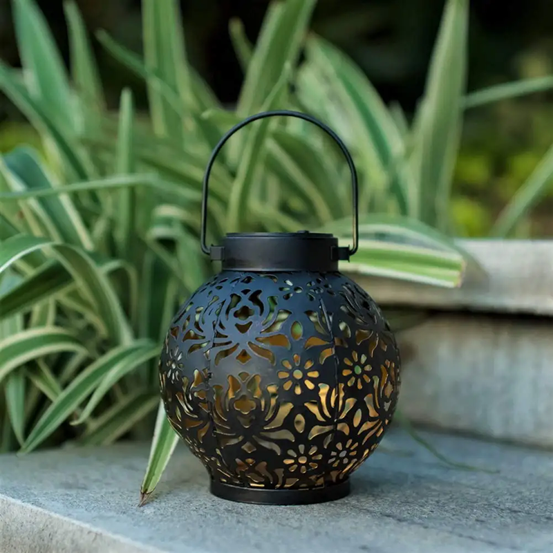 Decorative black lantern with floral patterns on a stone surface with green plants in the background