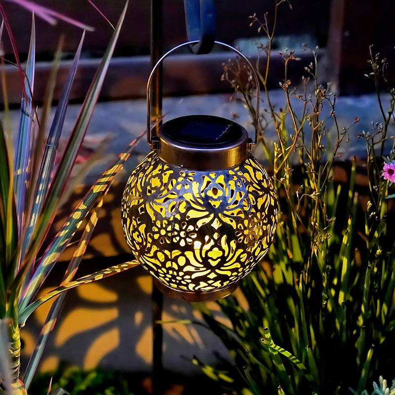 Decorative solar lantern with intricate design hanging among plants at night.