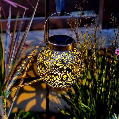 Decorative solar lantern with intricate design hanging among plants at night.