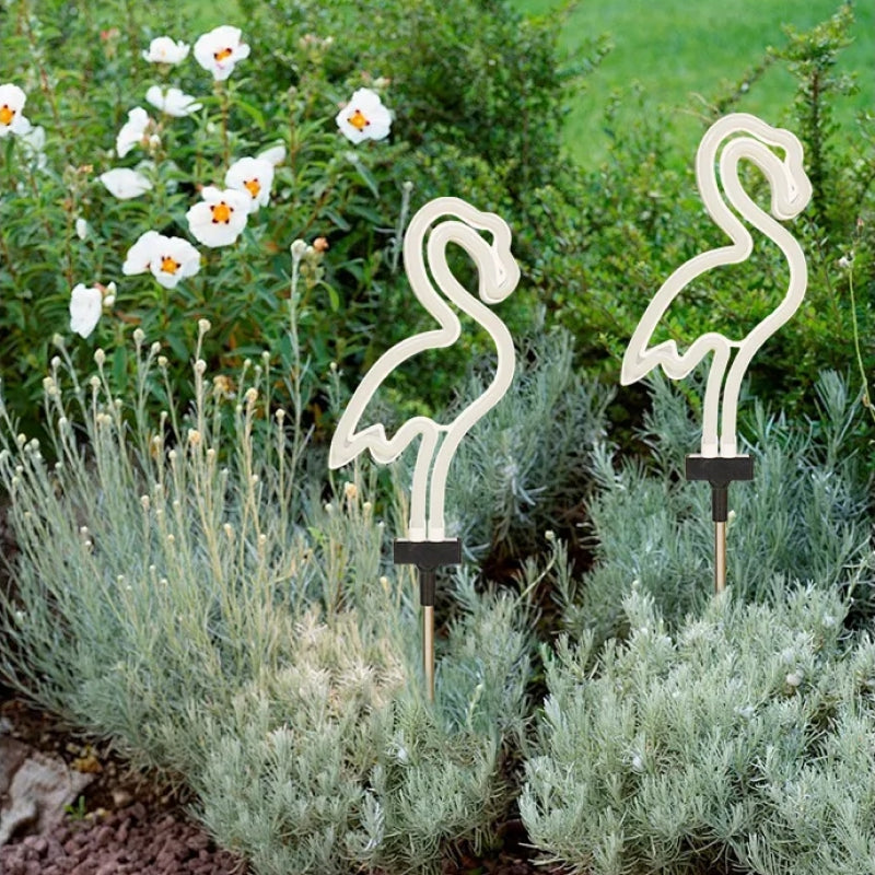 Flamingo-shaped garden lights in a garden setting with plants and flowers.