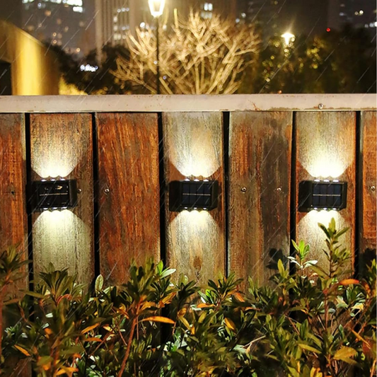 Solar-powered outdoor lights on a wooden fence with plants in the foreground.