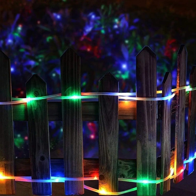 Colorful string lights on a wooden fence with a blurred colorful light display in the background.