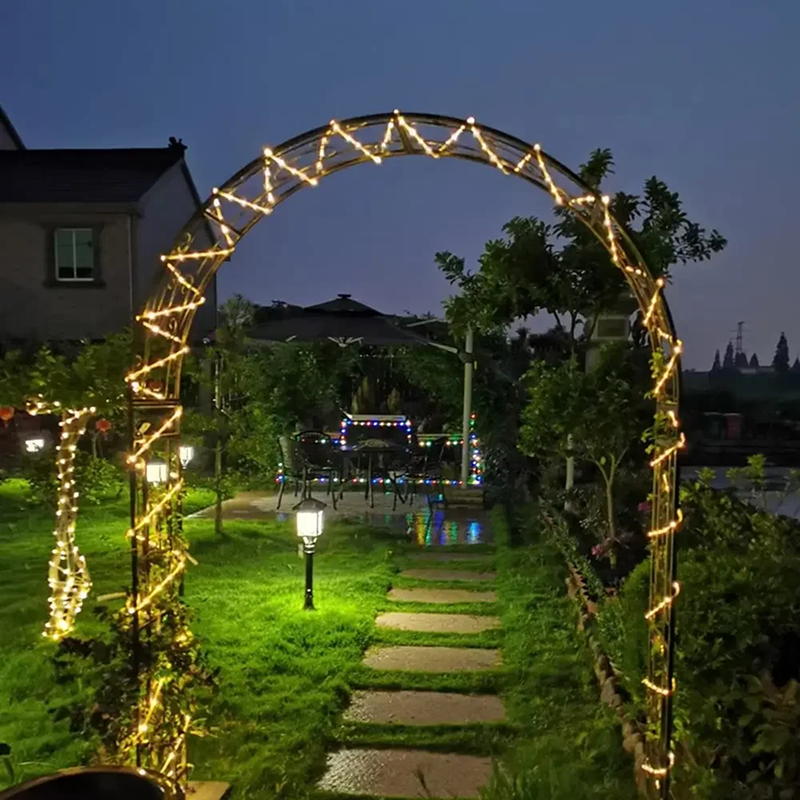 Decorative archway with string lights in a garden setting at night.