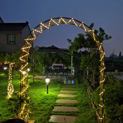 Decorative archway with string lights in a garden setting at night.