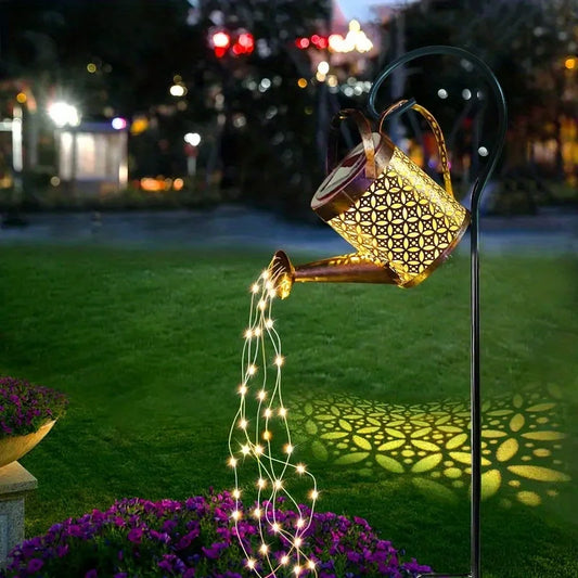 Decorative solar light shaped like a watering can casting a pattern on grass with flowers.