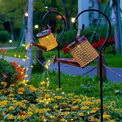 Decorative solar lights shaped like watering cans with string lights in a garden setting.