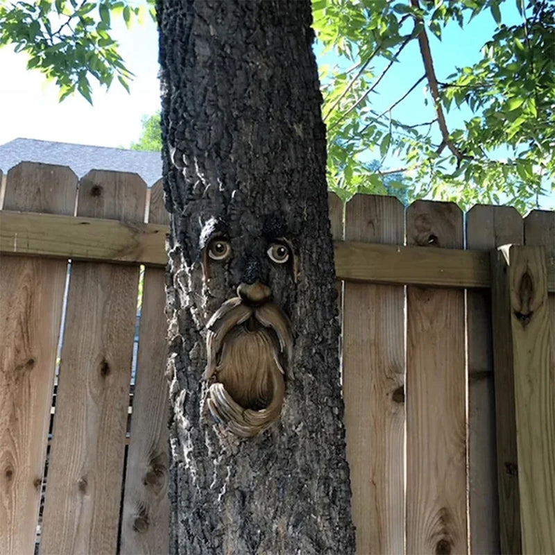Tree with a carved face against a wooden fence and greenery